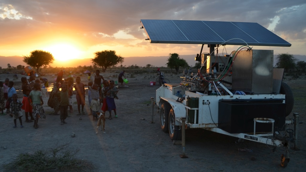Fahrzeuganhänger mit Solaranlage im Sonnenuntergang mit kleiner Menschengruppe
